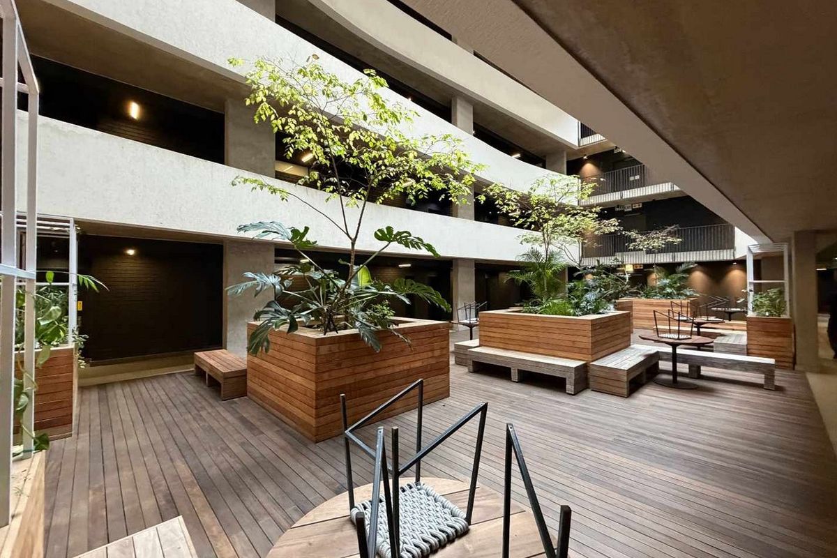 A modern, multi-level apartment complex courtyard featuring timber decking, built-in wooden planters, and open-air walkways.
