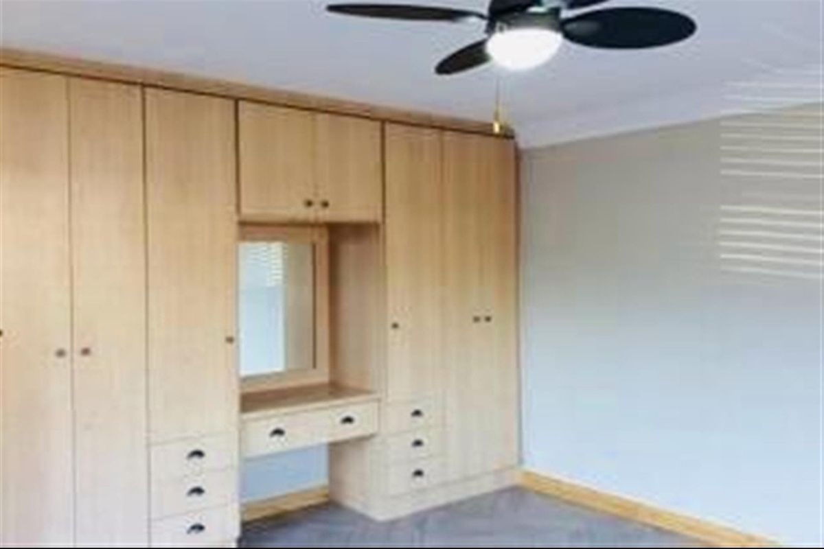 A bedroom featuring extensive built-in light wood cabinetry with an integrated vanity and mirror, complemented by a ceiling fan.