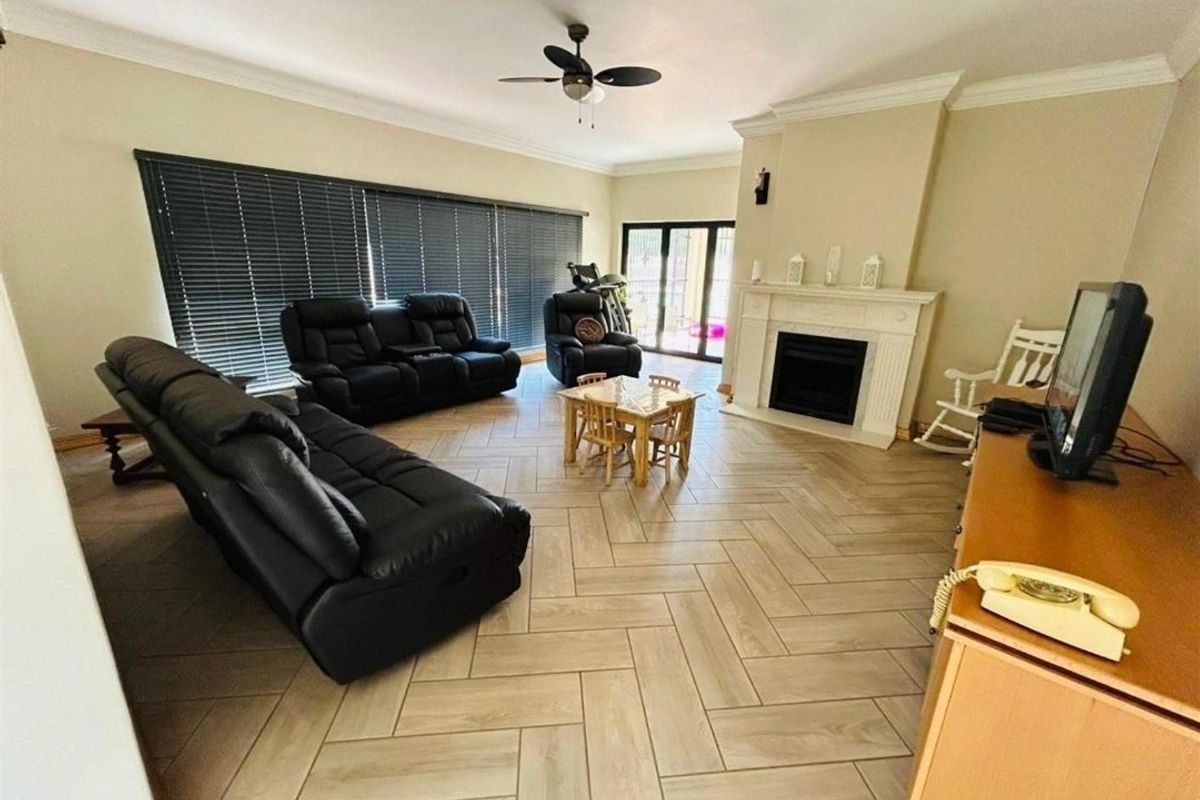 Spacious living room featuring herringbone-patterned tiled flooring, a built-in fireplace with a mantel, and large windows with fitted blinds.