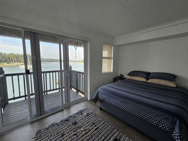 A bright bedroom featuring large sliding glass doors that open onto a private balcony with scenic water views.