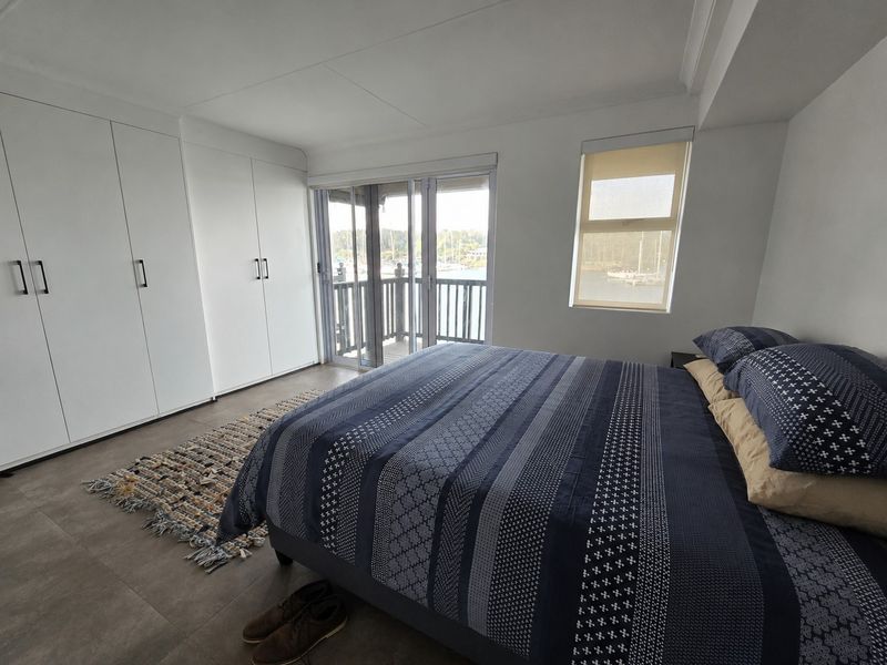 A bright bedroom featuring built-in floor-to-ceiling wardrobes, tiled flooring, and sliding glass doors opening onto a balcony with water views.