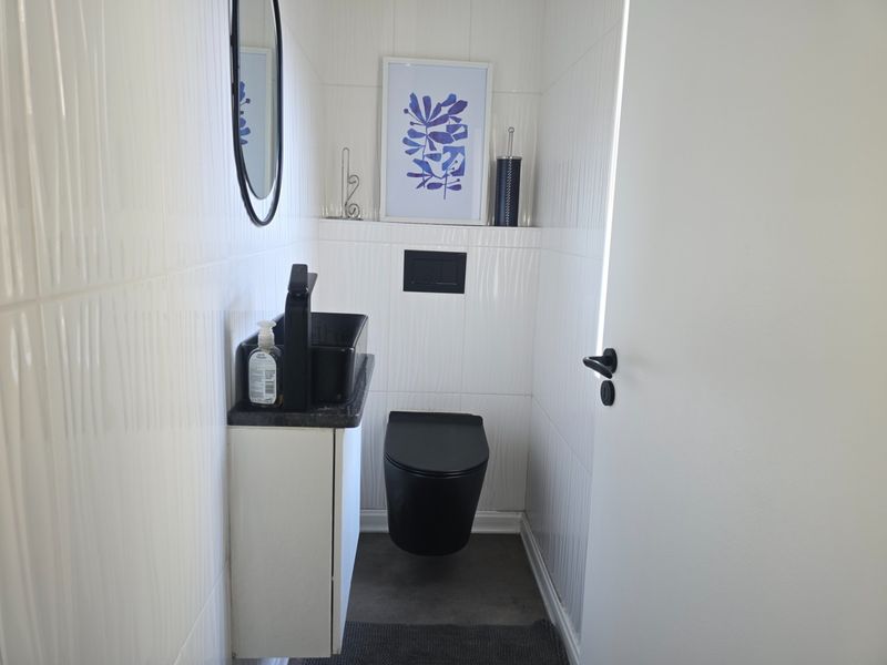 A modern guest bathroom featuring a wall-mounted toilet, a compact vanity with a black basin, and contemporary white tiled walls.