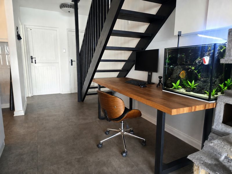 A functional home office space featuring a built-in wooden desk situated beneath a modern black staircase with matching railings and tiled flooring.