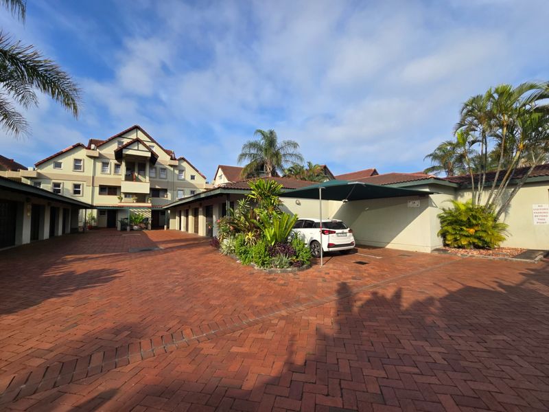 A view of the complex exterior featuring paved driveway, covered parking bays, and multi-story residential building architecture.