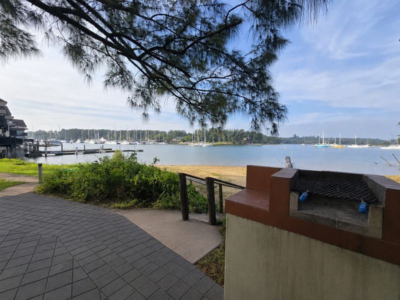 Outdoor waterfront area featuring a paved patio, built-in brick barbecue, and direct access to the water with scenic marina views.