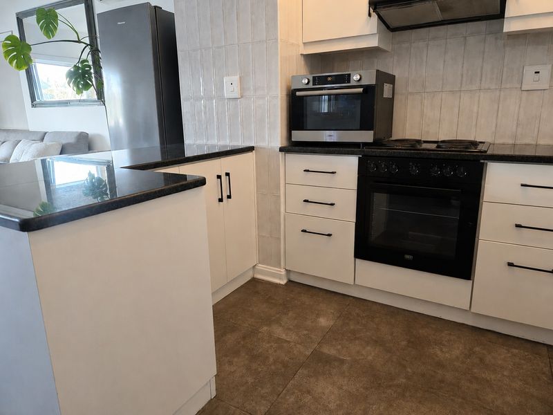 Modern kitchen featuring white cabinetry, dark granite countertops, built-in oven, hob, and extractor fan, with tiled flooring and a breakfast bar area.