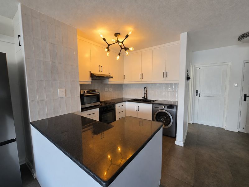 Modern kitchen featuring white cabinetry, dark granite countertops, integrated oven and hob, and a dedicated space for a washing machine.
