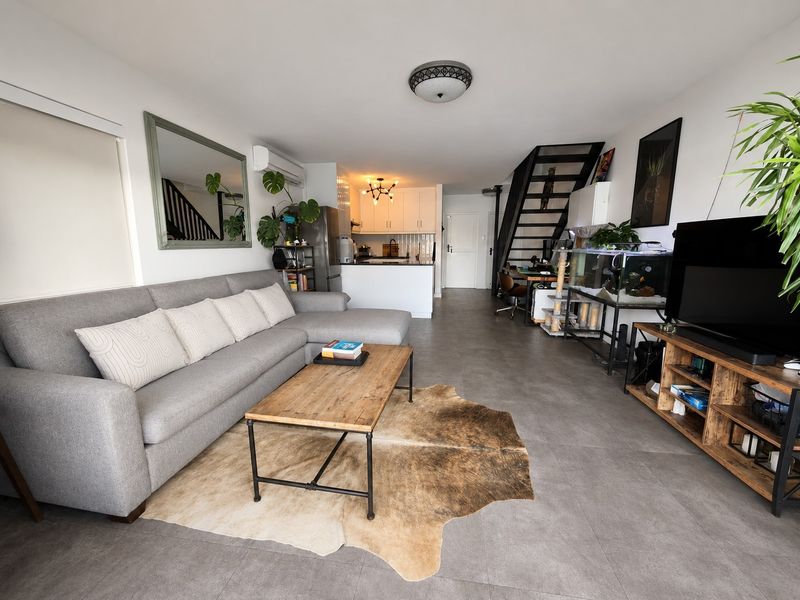 Open plan living area featuring tiled flooring, a modern kitchen with white cabinetry, and a staircase leading to the upper level.