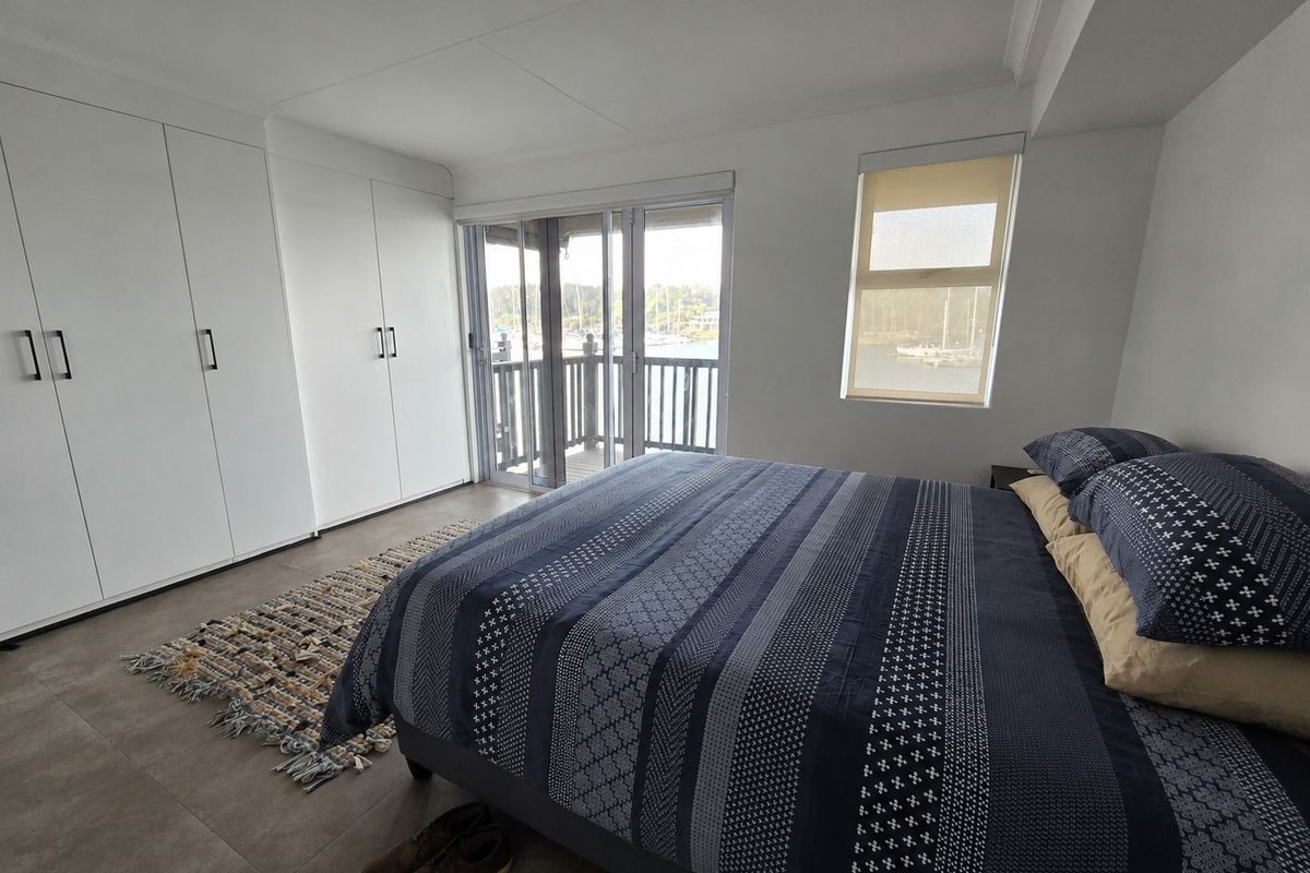 A bright bedroom featuring built-in floor-to-ceiling wardrobes, tiled flooring, and sliding glass doors opening onto a balcony with water views.