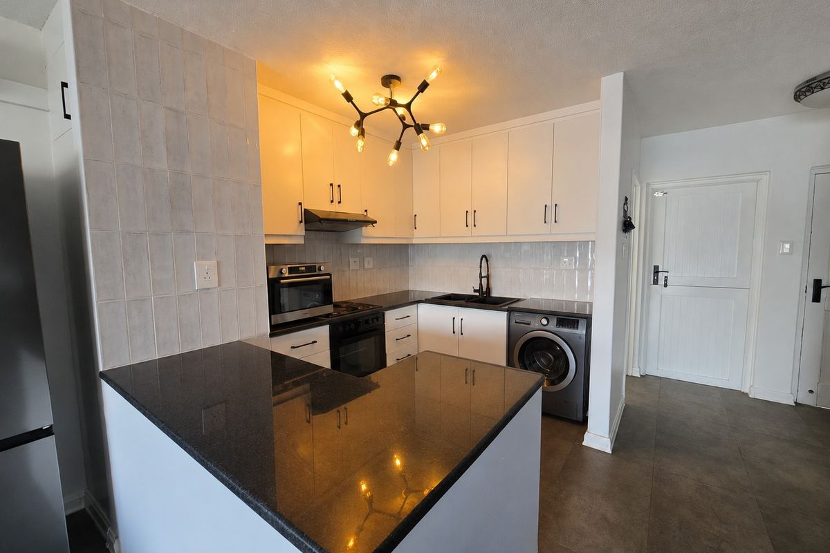 Modern kitchen featuring white cabinetry, dark granite countertops, integrated oven and hob, and a dedicated space for a washing machine.