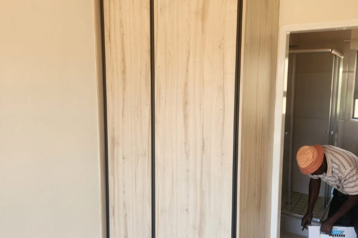 A bedroom featuring a modern, light wood-grain built-in wardrobe with sliding doors, adjacent to an en-suite bathroom.