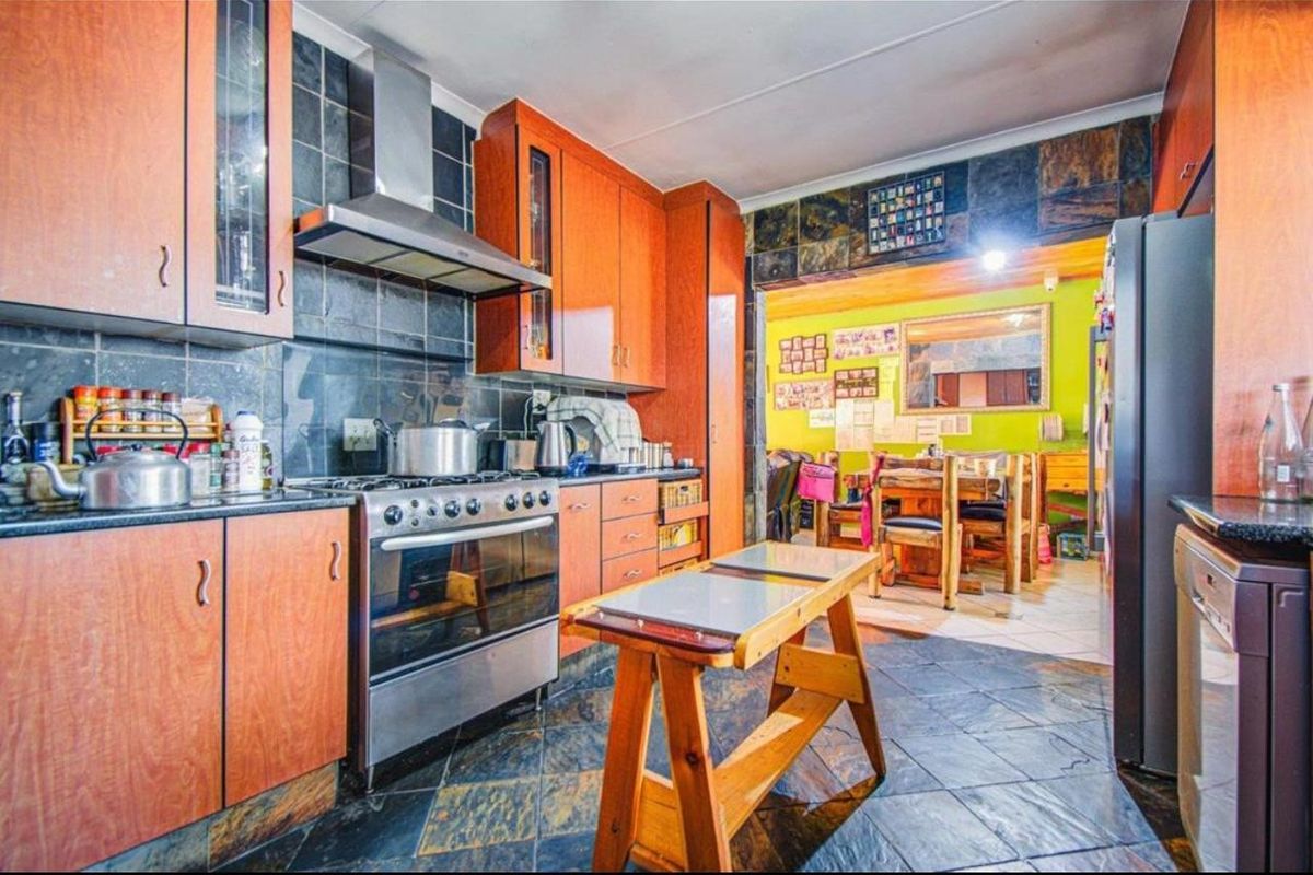 A functional kitchen featuring wooden cabinetry, a stainless steel gas stove with extractor fan, and dark slate tile flooring, opening into an adjacent dining area.
