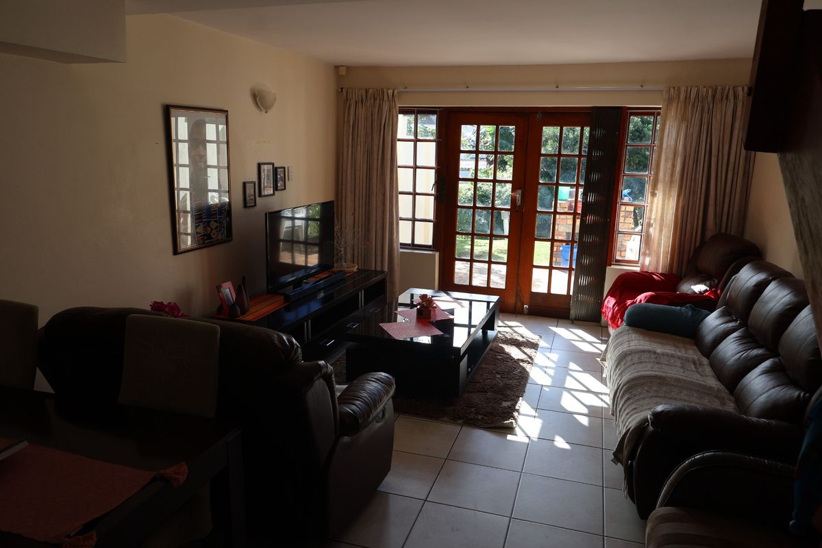 A comfortable living room featuring tiled flooring and large wooden-framed glass doors that provide direct access to the outdoor patio area.