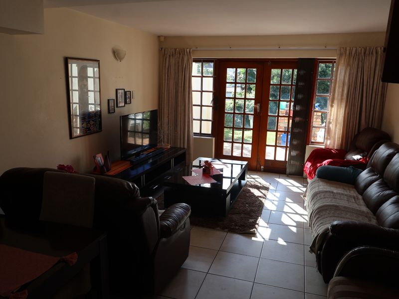 A comfortable living room featuring tiled flooring and large wooden-framed glass doors that provide direct access to the outdoor patio area.
