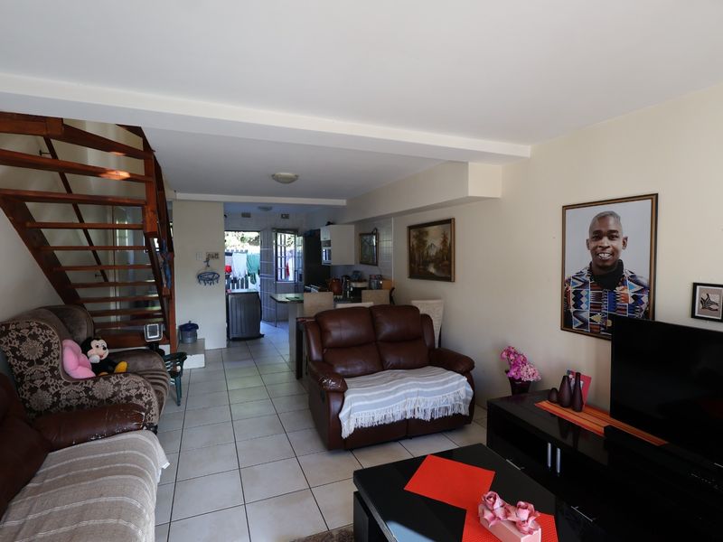 Open plan living area featuring tiled flooring and a wooden staircase leading to the upper level, with a kitchen visible in the background.