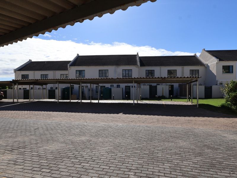 Exterior view of a townhouse complex featuring a paved parking area with covered carports and a row of residential units.