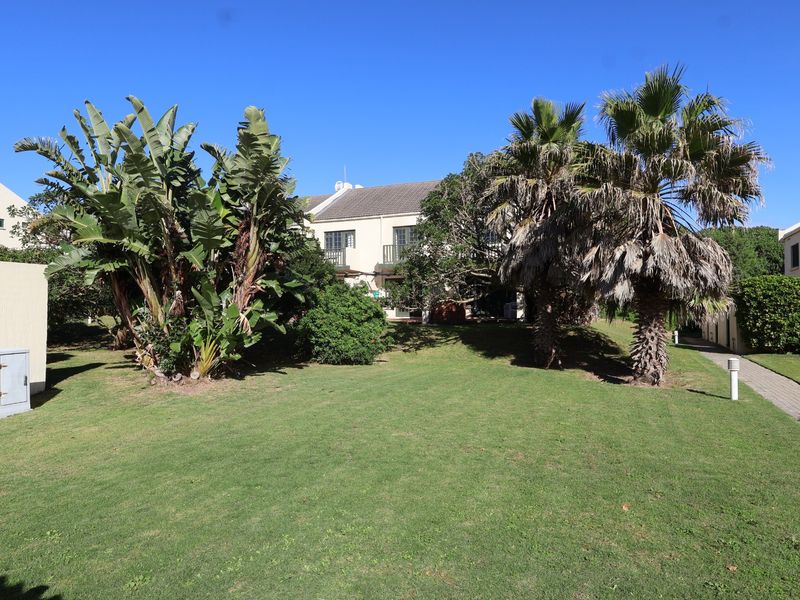 A view of the rear exterior of the townhouse, featuring a well-maintained lawn, mature palm trees, and paved pathways.