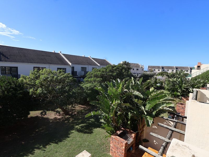 Elevated view overlooking a communal garden area with mature trees, featuring a private balcony with a built-in brick braai and timber pergola structure.