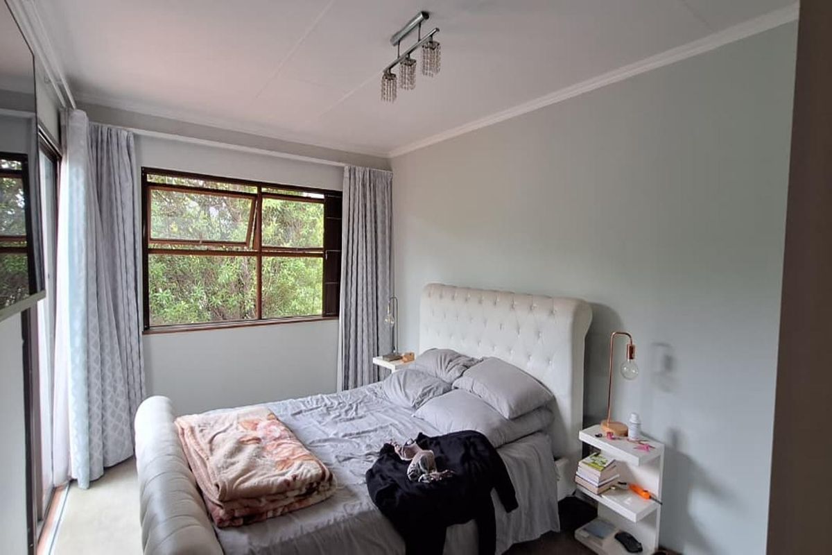 A well-lit bedroom featuring neutral wall tones, a large window with garden views, and a sliding door providing access to the exterior.