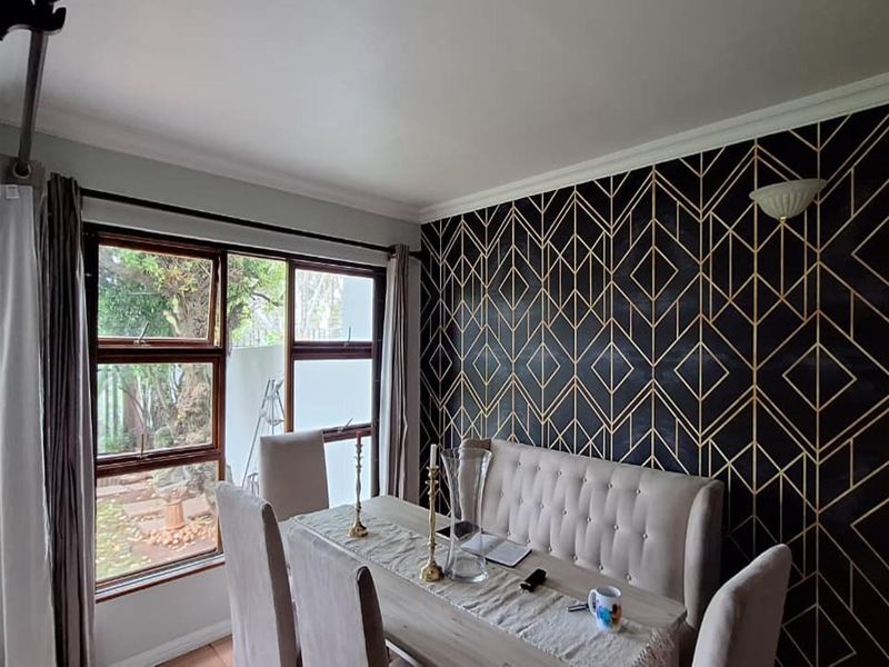 A well-lit dining room featuring a striking geometric feature wall, large windows providing natural light, and classic coving detail.