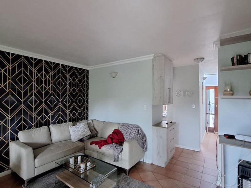 A living room featuring tiled flooring, built-in cabinetry, and a decorative feature wall, providing a functional and well-defined living space.