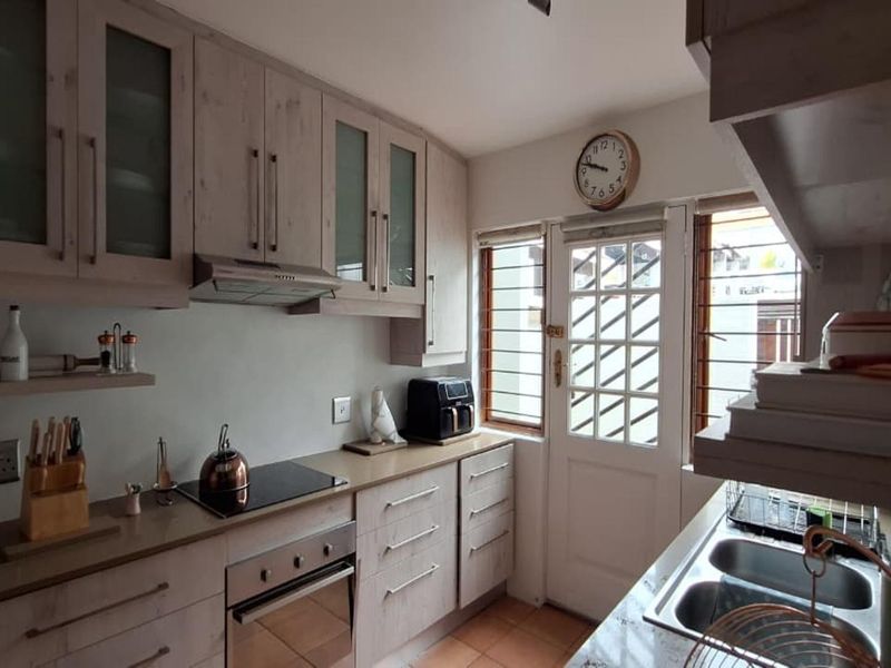 A functional kitchen featuring light wood-toned cabinetry, integrated appliances including an electric hob and oven, and direct access to the exterior via a security door.