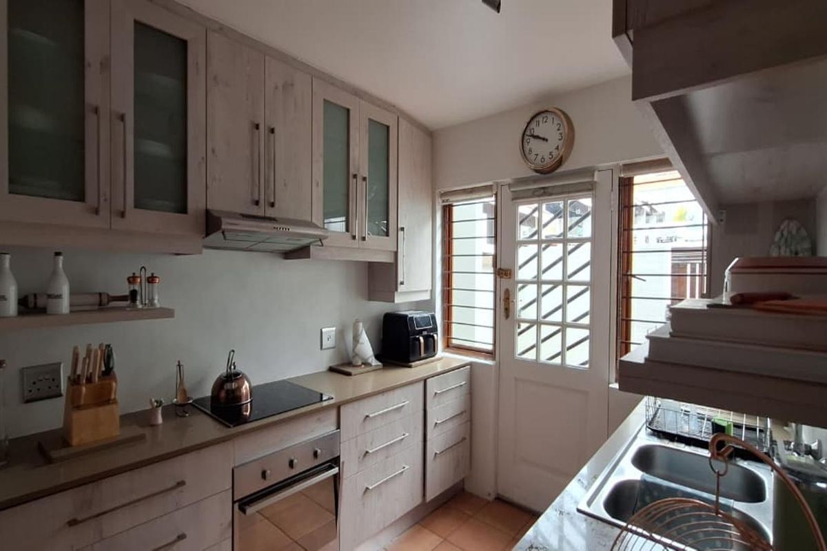 A functional kitchen featuring light wood-toned cabinetry, integrated appliances including an electric hob and oven, and direct access to the exterior via a security door.