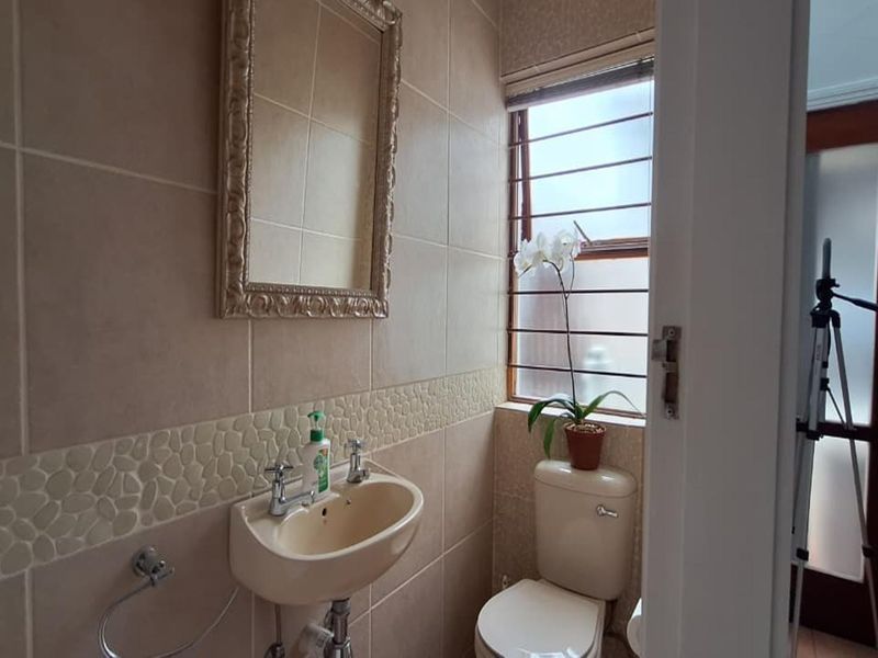 A compact guest bathroom featuring tiled walls, a wall-mounted basin, and a toilet, with natural light provided by a window with security bars.