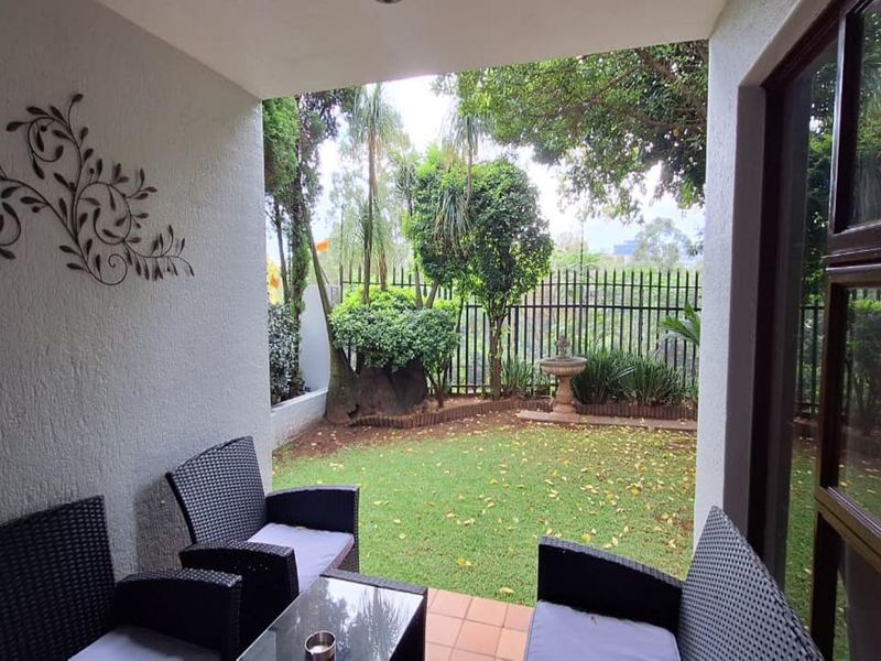 A covered patio area overlooking a private garden with a small fountain and secure perimeter fencing.