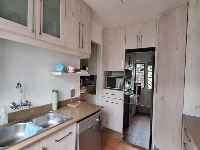 A functional kitchen featuring light wood-grain cabinetry, double stainless steel sink, integrated dishwasher, and built-in microwave with tiled flooring.