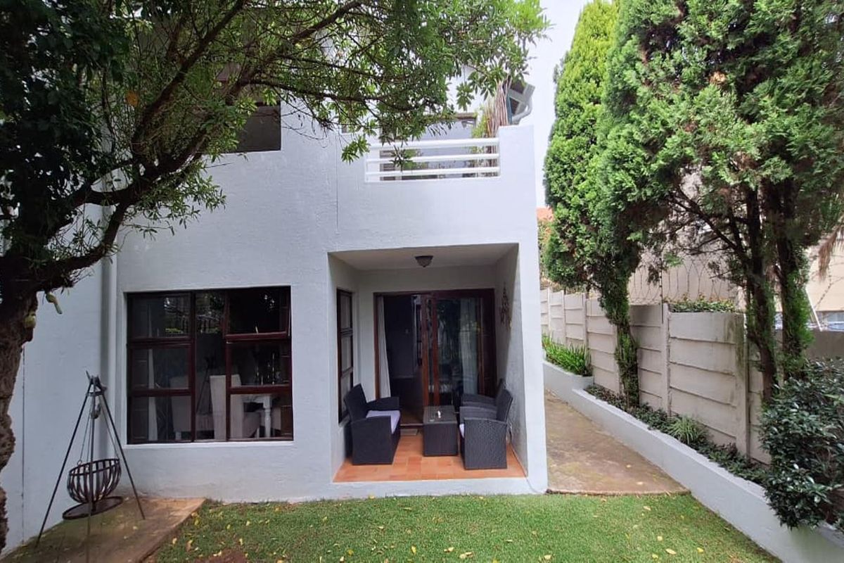 Rear view of the property featuring a covered patio, an upper-level balcony, and a private garden area with established trees and boundary walling.