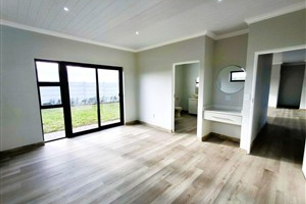 Spacious bedroom featuring light wood-look flooring, recessed ceiling lighting, a built-in vanity area, and sliding glass doors leading to the exterior.