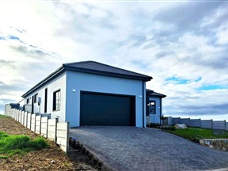 Modern single-story house exterior featuring a paved driveway, integrated garage, and perimeter boundary walling under a clear sky.