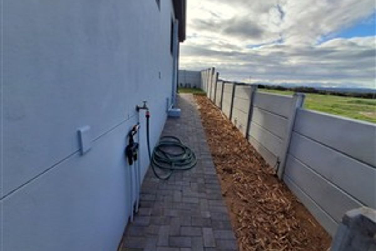 Side exterior walkway featuring paved path, concrete boundary wall, and external water tap connection.