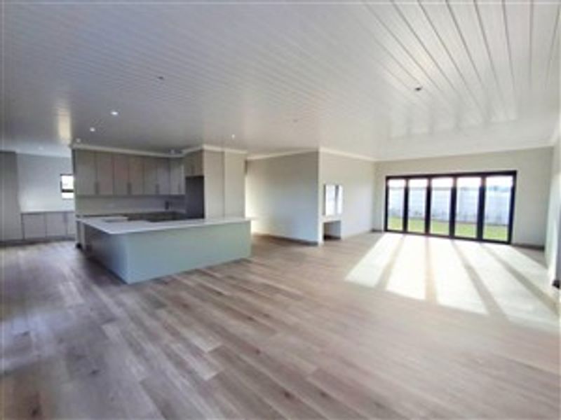 Spacious open-plan living area featuring light timber flooring, a modern kitchen with a central island, and large folding doors leading to the garden.