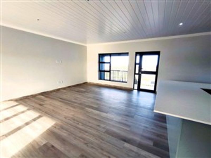 Spacious open-plan living area featuring modern wood-look flooring, recessed lighting, and direct access to an outdoor balcony through a glass door.