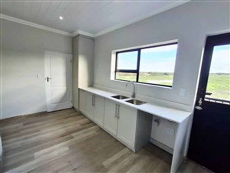 A modern, minimalist kitchen area featuring sleek white cabinetry, a stainless steel sink, and light wood-look flooring with direct outdoor access.