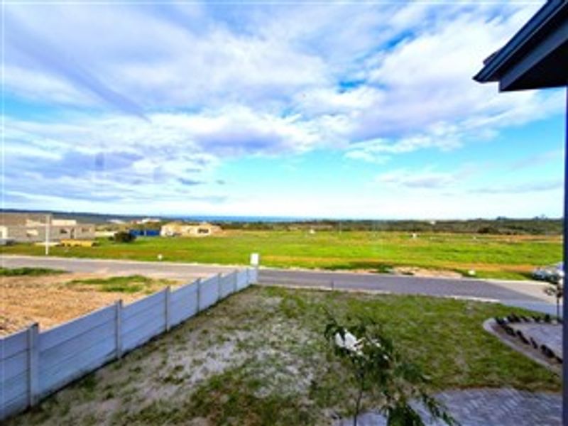 An elevated view overlooking a vacant plot of land and surrounding neighborhood with distant sea views.