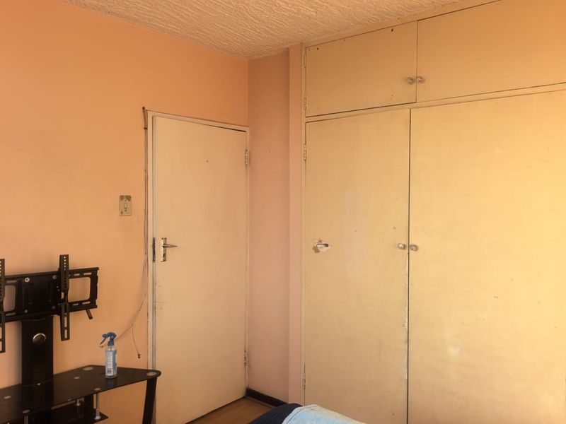 A bedroom featuring built-in floor-to-ceiling cupboards and a standard interior door, requiring cosmetic updates to the wall finishes and cabinetry.