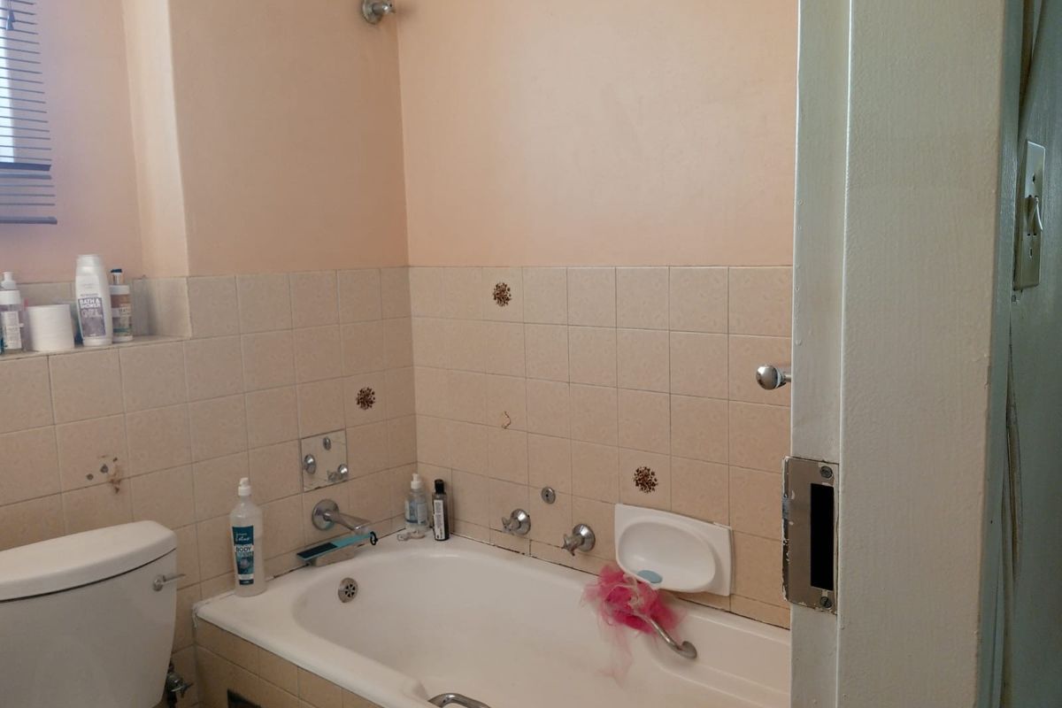 A dated bathroom featuring a built-in bathtub with wall-mounted mixer taps, a ceramic toilet, and tiled splashbacks.