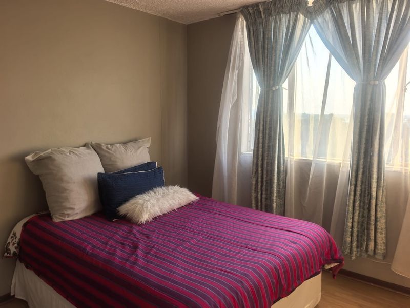 A bedroom featuring neutral wall tones, laminate flooring, and a large window with curtain treatments.