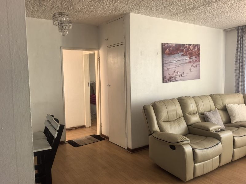 A living area featuring laminate flooring, a built-in storage cupboard, and access to an adjacent room.