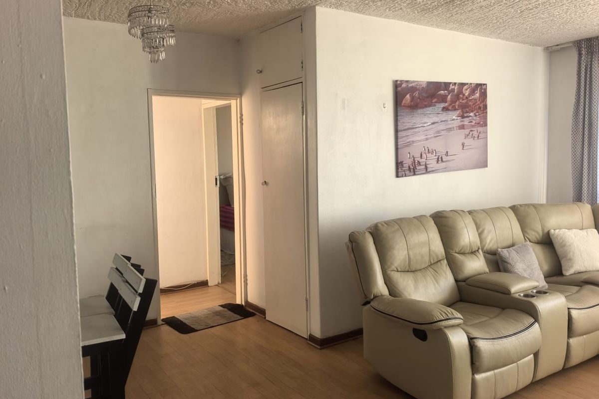 A living area featuring laminate flooring, a built-in storage cupboard, and access to an adjacent room.