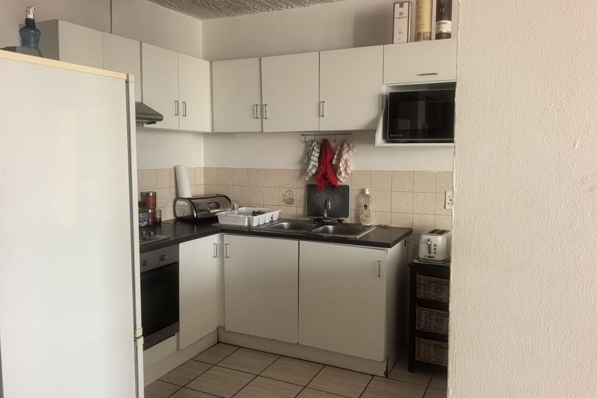 A functional kitchen featuring white cabinetry, a built-in oven, extractor fan, and tiled flooring, offering a practical layout for daily meal preparation.