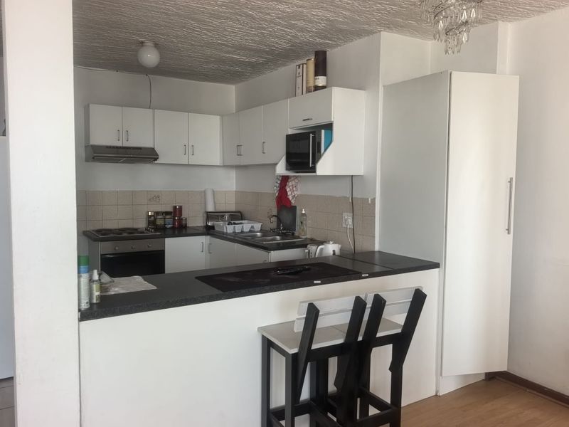 Compact kitchen featuring white cabinetry, a built-in oven and hob, tiled backsplash, and a breakfast bar counter.