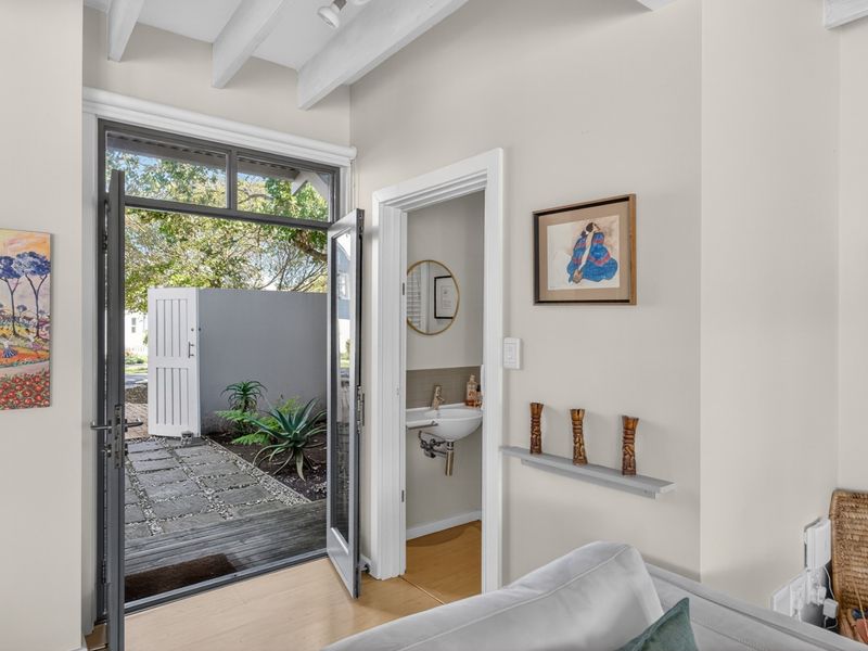 An interior view showing an entrance with exposed ceiling beams, leading to a small powder room and an outdoor patio area.