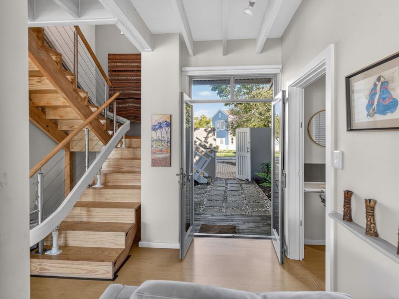 Bright entrance foyer featuring a timber staircase with stainless steel balustrades, leading to an outdoor paved courtyard area.