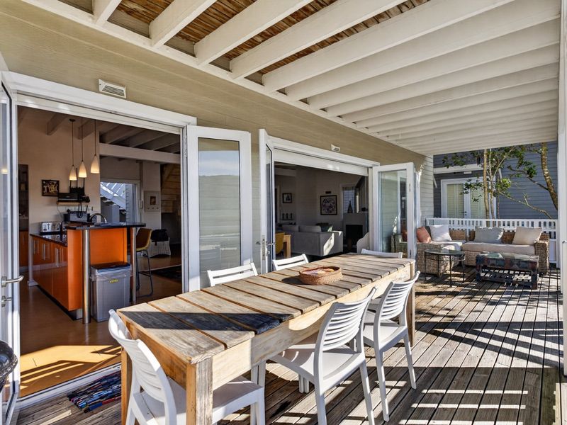Spacious covered timber deck featuring an outdoor dining area, seamlessly connecting to the open-plan kitchen and living space through large folding glass doors.