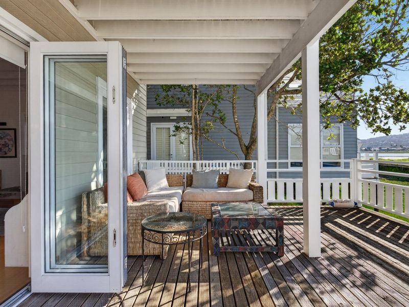 A covered outdoor patio featuring timber decking, white structural posts, and bi-fold doors providing seamless indoor-outdoor flow.