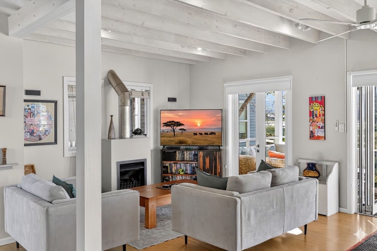 Bright living room featuring exposed timber beam ceilings, a built-in fireplace with a metal flue, and direct access to an outdoor patio area.